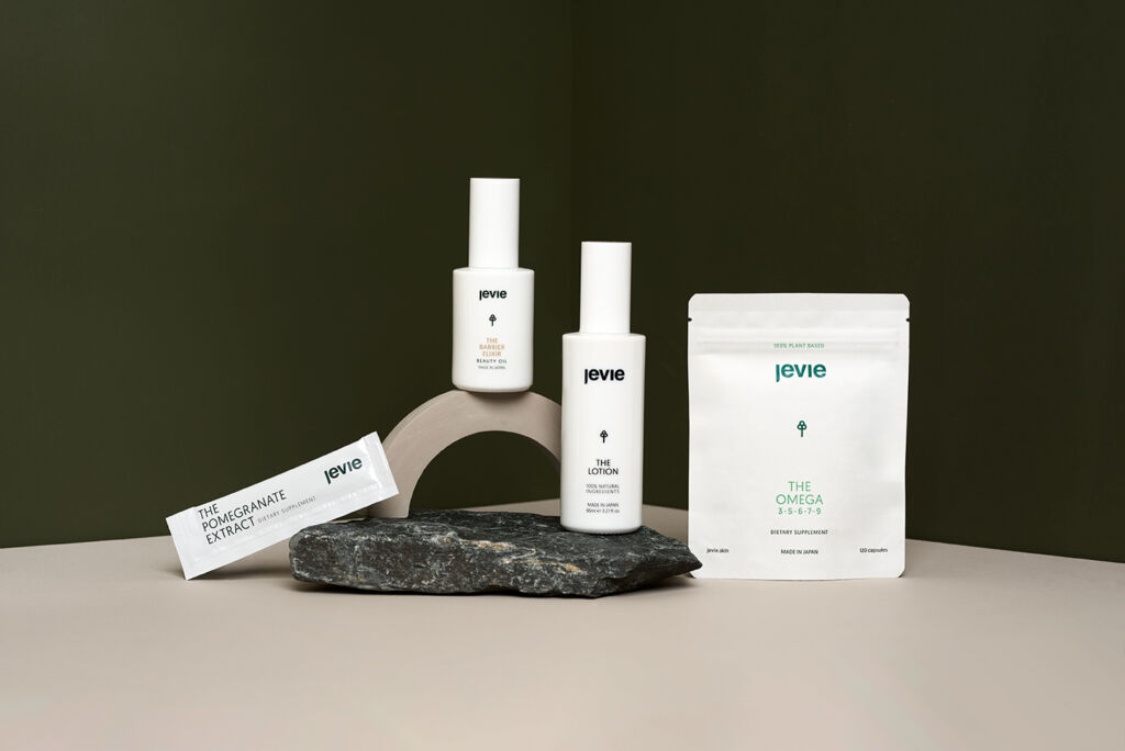 4 White products placed in a cornered space with two green walls and a taupe floor. Two products are leaning on a rock and one stands on an arch.