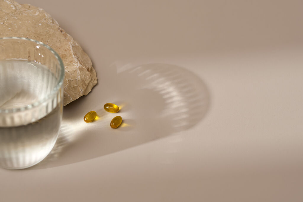 A glass with water where comes light through which gives a reflection on the pills that are lying right next to the water glass.