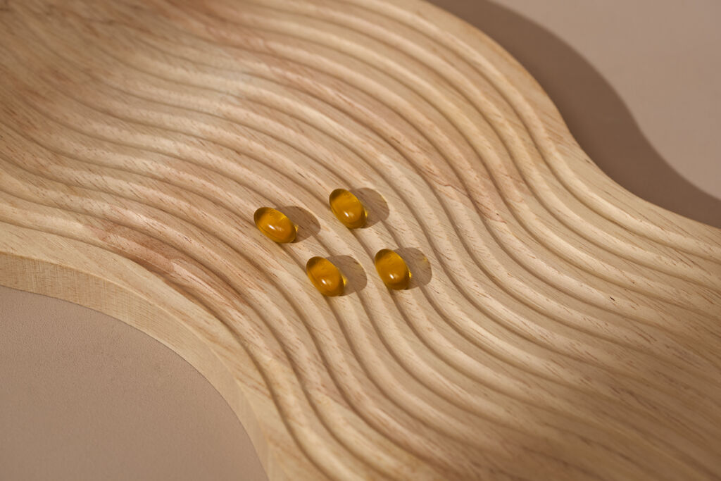 4 Pills on a wooden wave board. The light is shining through the pills which gives a warm reflection onto the wood.