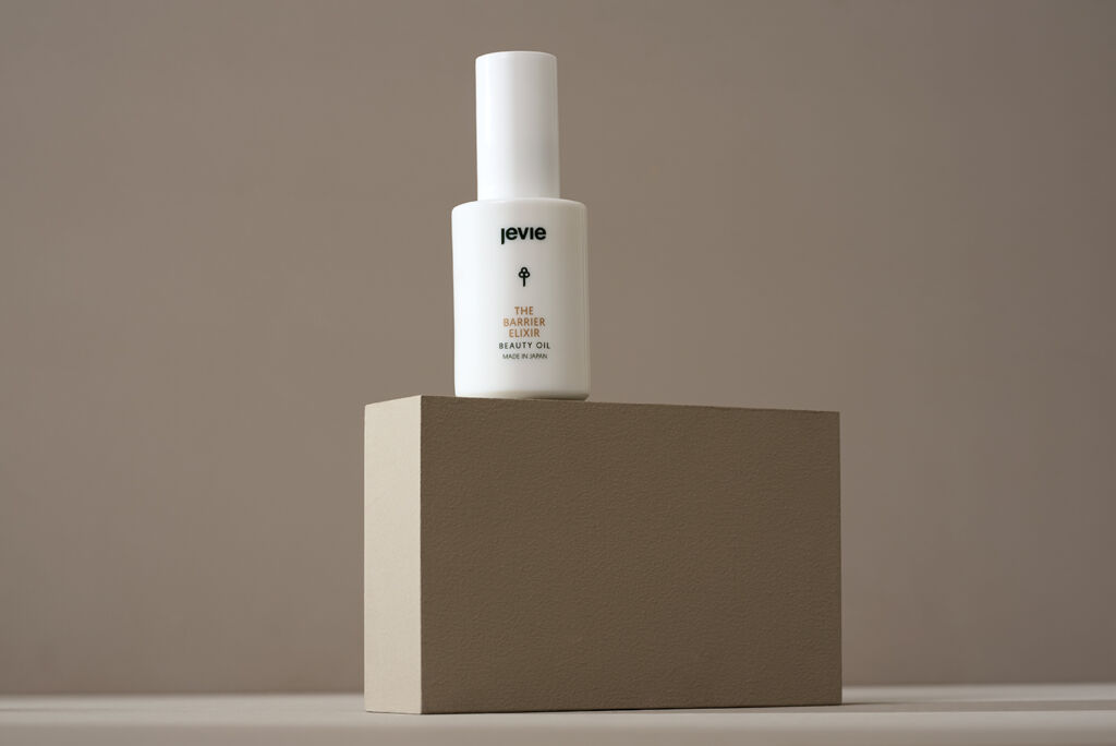 The Barrier Elixer. Placed on a taupe background, with lighting on the side which is lighting up the block the product is placed on. 